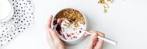 Person-Mixing-Cereal,-Milk,-and-Strawberry-Jam-on-White-Ceramic-Bowl